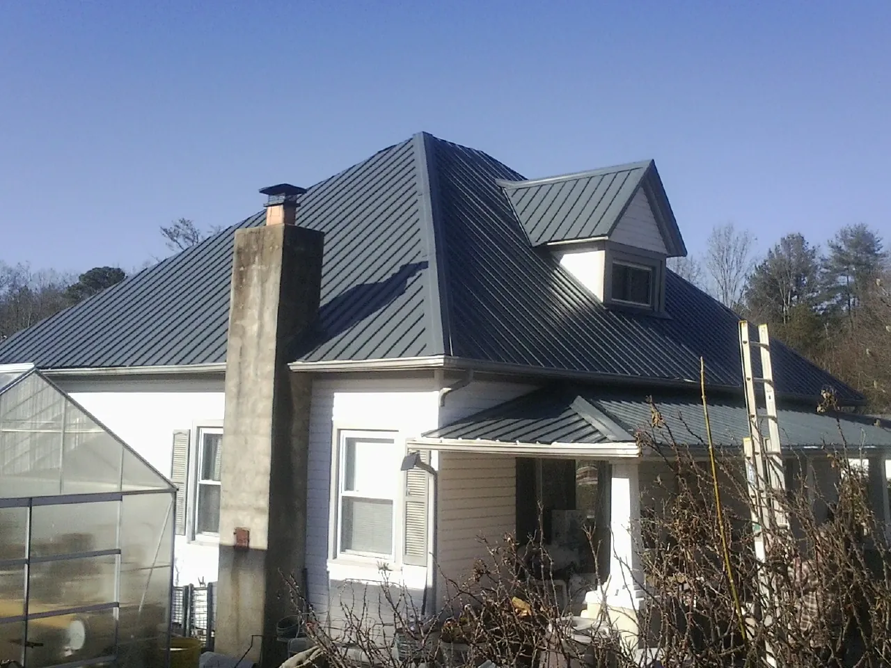 Dark blue standing seam metal roof on a white farmhouse with dormer — Slate & Tile Roof Repair by Roofing Brothers in Dunnellon