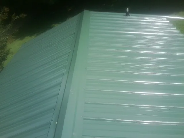 New green metal panels meeting at the ridge of a roof — Flat Roof Repair work by our crew in Dunnellon