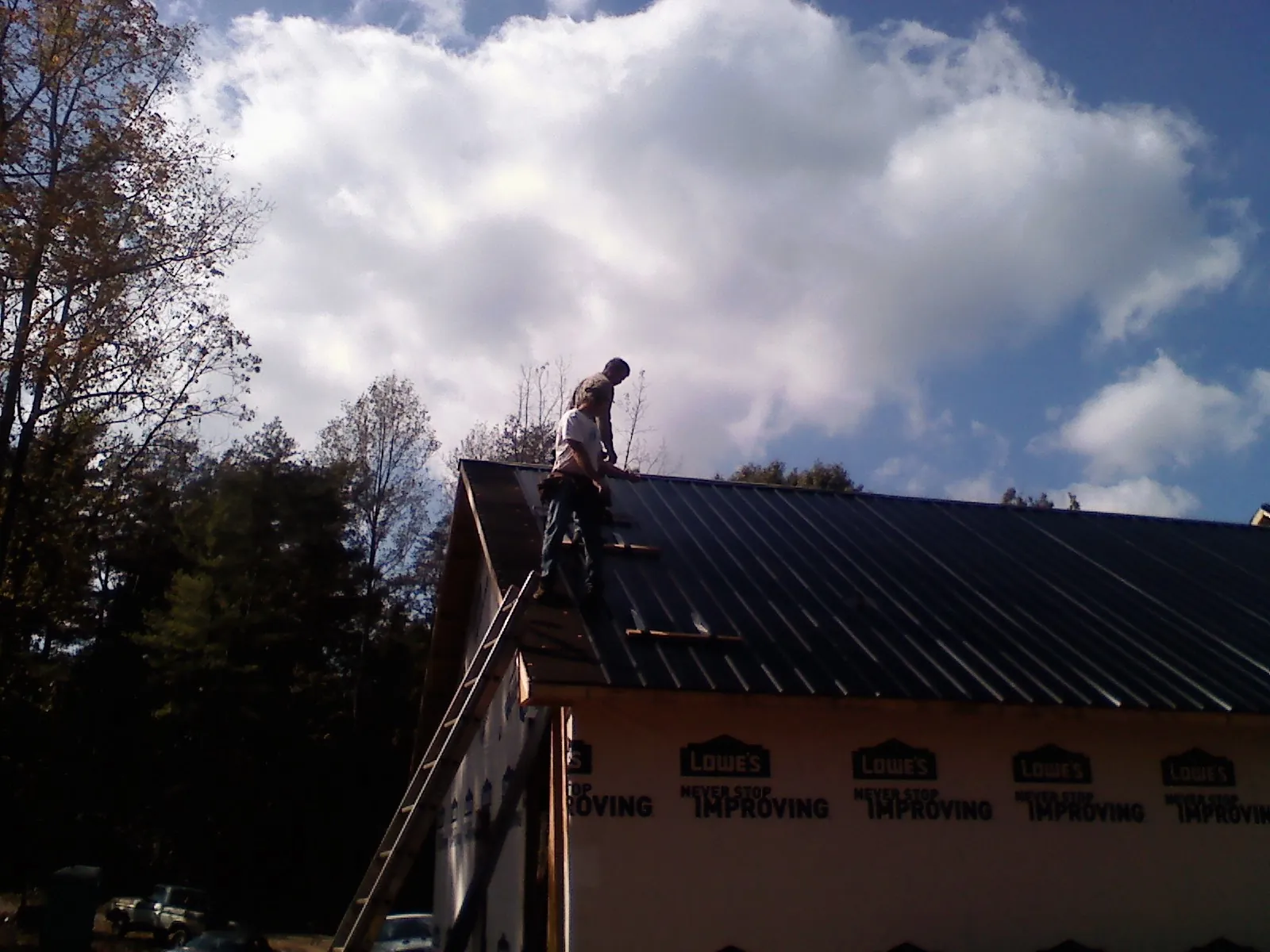 Roofer fastening dark metal panels high against a cloudy sky, from a Roof Inspection job in Dunnellon