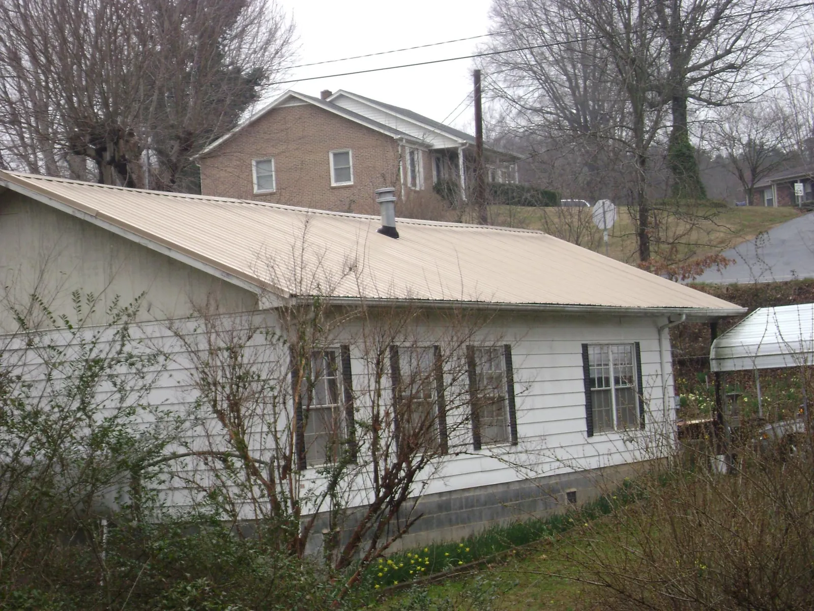 Tan metal roof on a white sided house set into a hillside — Commercial Roofing by Roofing Brothers in Dunnellon